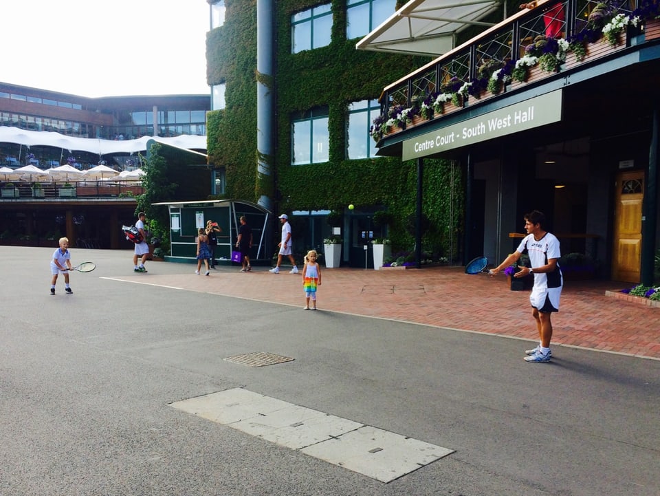 ein Tennisspieler spielt vor dem Center Court mit zwei Kindern.