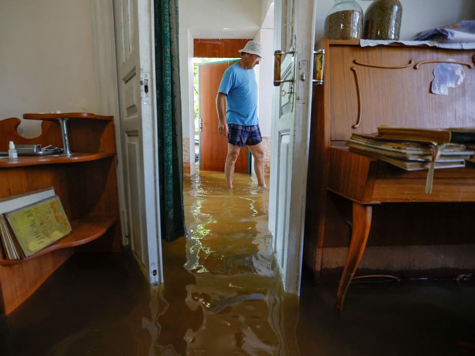 Ein Mann läuft in einem Gang eines Hauses. Der Boden ist knöchelhoch mit Wasser bedeckt.