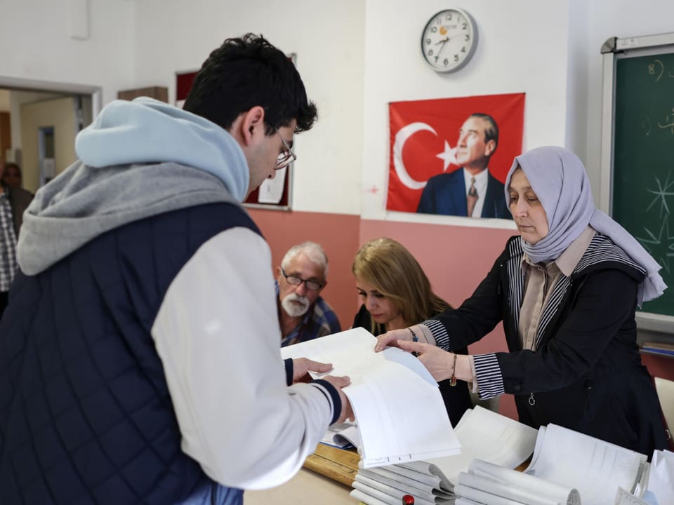 Ein Mann bezieht in einem Wahllokal in Istanbul die Wahlunterlagen. Eine Frau händigt ihm sie aus.