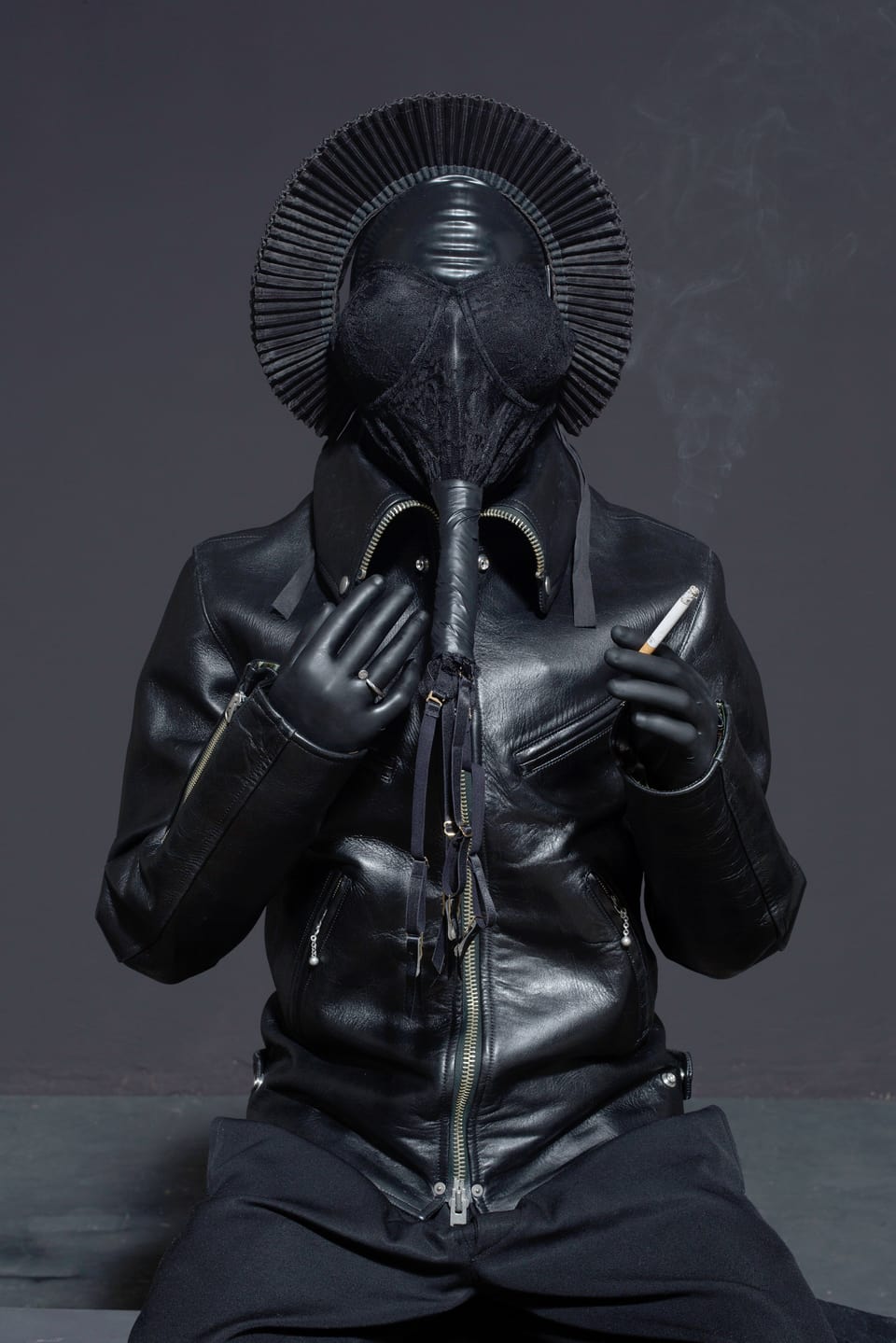 Eine ganz in schwarz mit schwarzer Maske bekleidete Person, die eine Zigarette raucht.