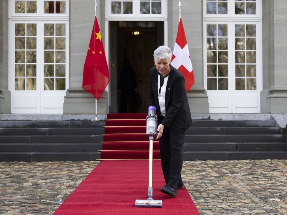 Eine Mitarbeiter mit dem Staubsauer auf dem roten Teppich, im Hintergrund die Schweizer und die chinesische Flagge.