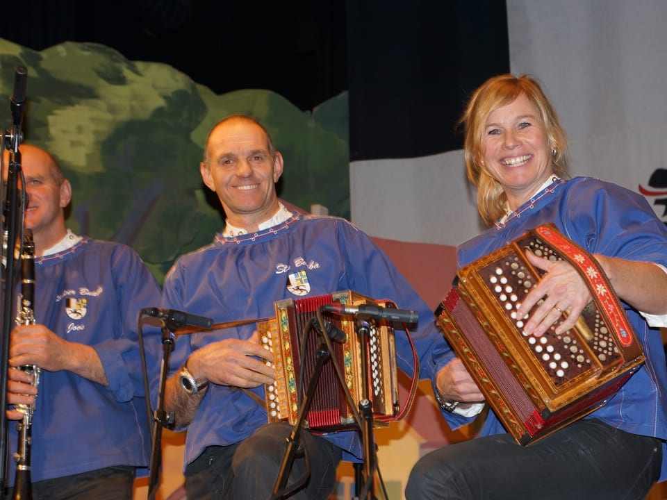Zwei Männer und eine Frau in blauen Sennenhemden beim Musizieren.