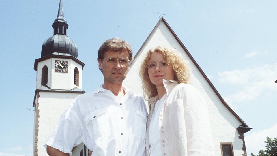 Maren Kroymann und Robert Atzorn stehen vor einem Kirche.