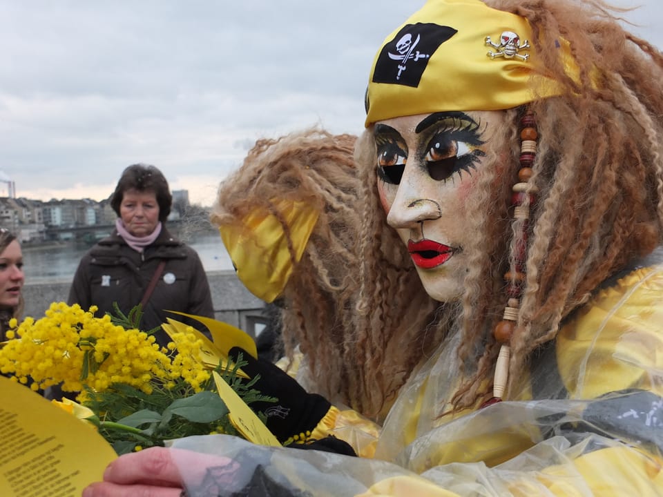 Gelbe Larve mit gelbem Zeedel und Mimose in der Hand.