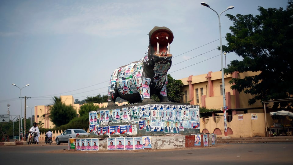 Eine Verkehrsinsel, auf der ein grosses Nilpferd aus Stein steht, ist vollgekleistert mit Wahlplakaten.