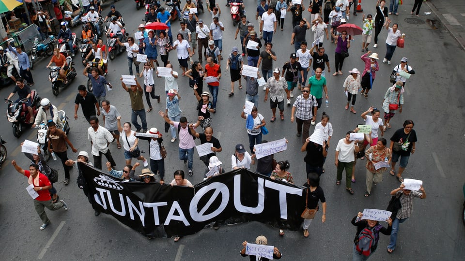 Menschen halten Plakate und Transparente in die Höhe und laufen durch eine Strasse in Bangkok.