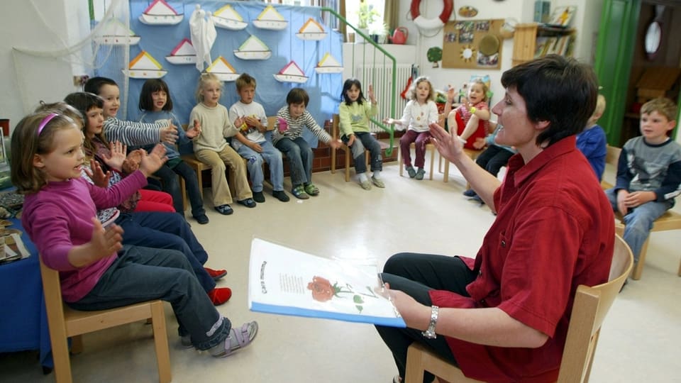 Eine Kindergärtnerin liest kleinen Kindern im Kreis Geschichten vor
