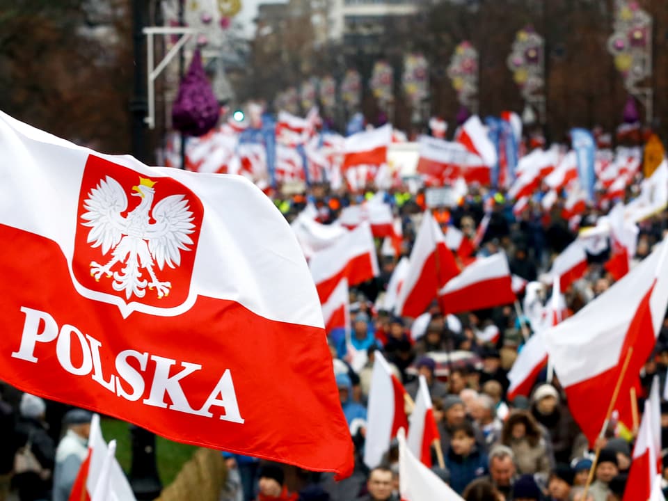 Eine Demonstration mit weiss-roten Fahnen, im Vordergrund eine Fahne mit der Aufschrift "Polska".