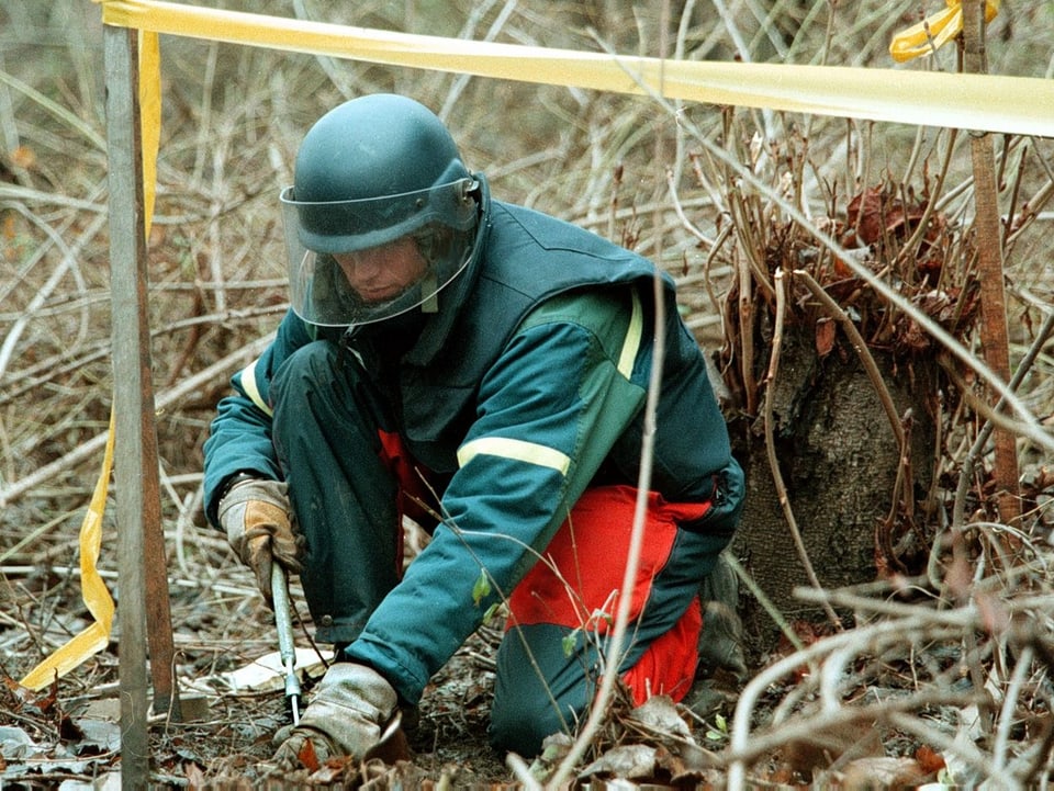 Ein Mann im grünen Schutzanzug entschärft eine Mine in Bosnien.