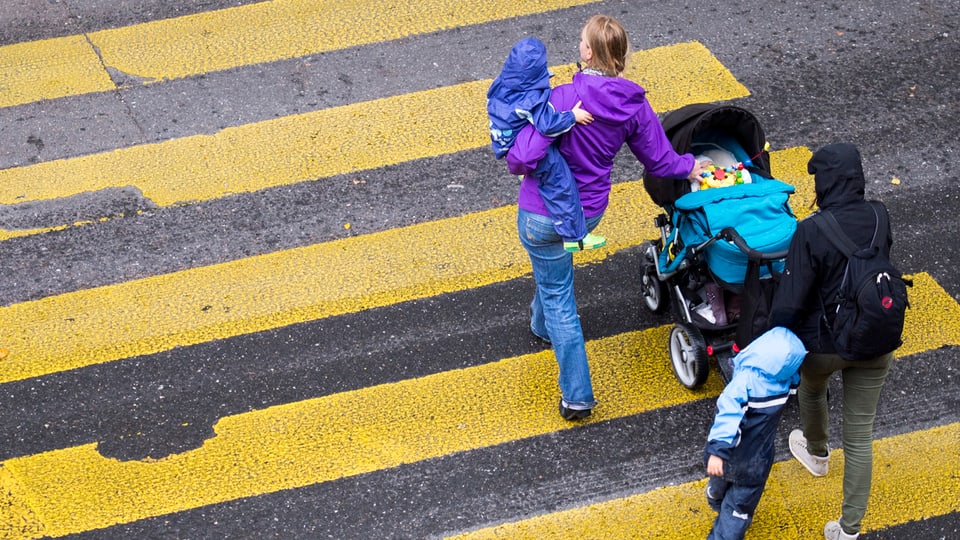 Zwei Frauen gehen mit einem Kinderwagen und zwei Kindern über den Fussgängerstreifen.