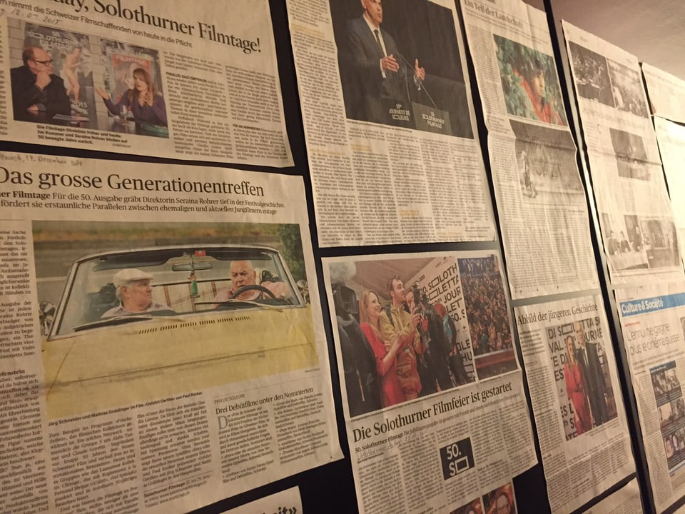 Zeitungsseiten sind an eine Wand geheftet.