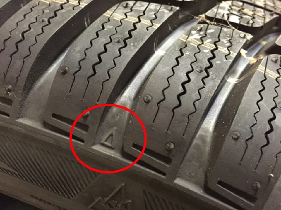 Nahaufnahme eines Reifenprofils, worauf ein kleiner Pfleil sichtbar ist.
