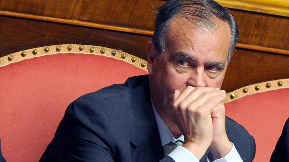 Calderoli sitzt im Parlament und hält seine Hände geschlossen vor dem Mund. 