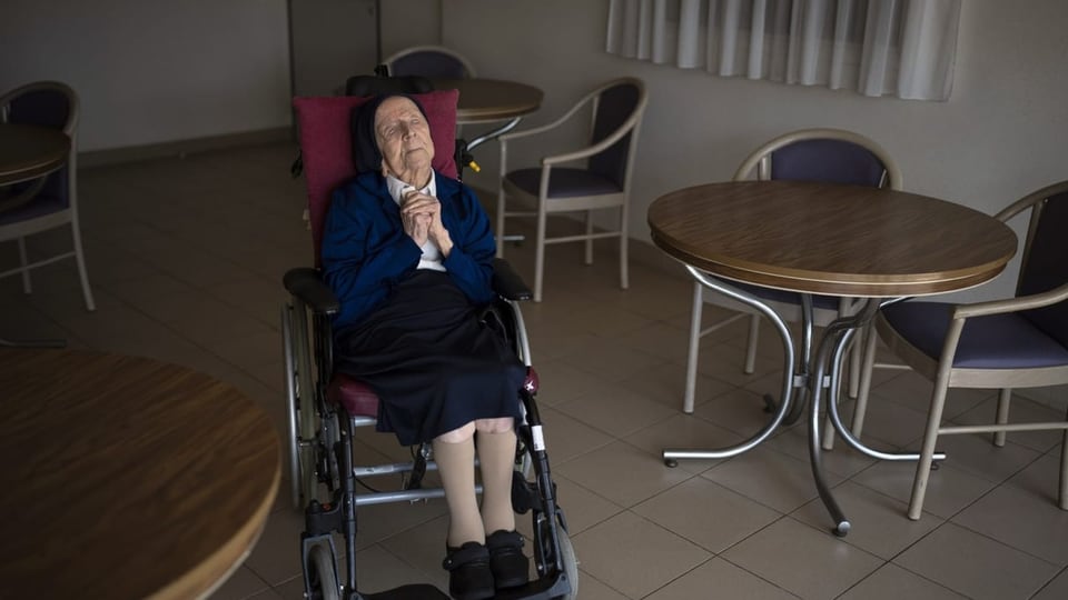 Eine betende alte Frau im Rollstuhl