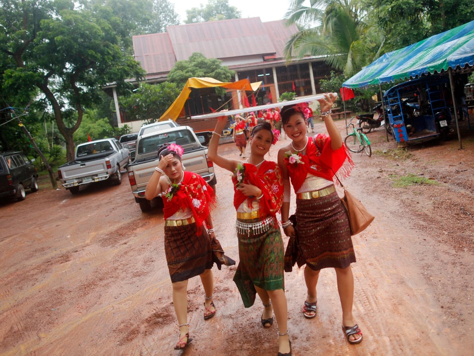 Junge Frauen in traditioneller roter Kleidung gehen auf einer Dorfstrasse