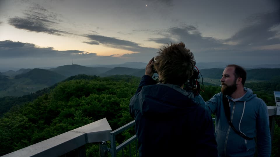 Die hügelige Landschaft des Aargauer Juras im Hintergrund im Morgenlicht, vorne der Kameramann mit Assistent. 