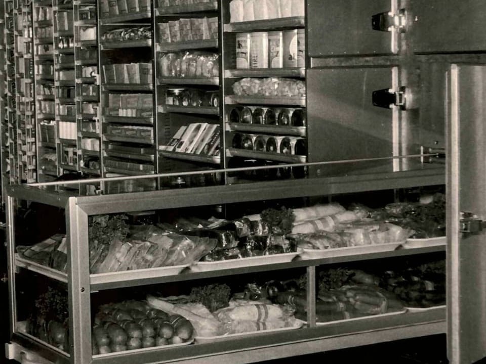 Schwarz-weiss-Foto von vollständig gefüllten Lebensmittelregalen in einem Geschäft.