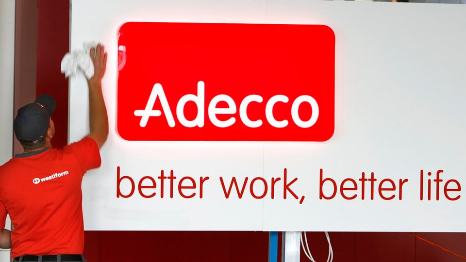 Angestellter einer Reinigungsfirma putzt das Adecco-Logo an einem Firmengebäude