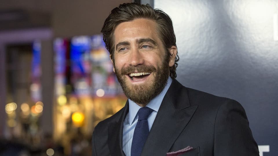 Jake Gyllenhaal trägt einen schwarzen Anzug und lacht. 