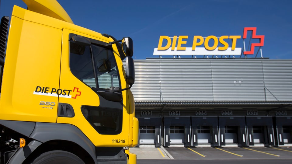 Gelber Lastwagen der Post mit Logo vor dem Paketzentrum Härkingen, auf dessen Dach ebenfalls ein Post-Logo angebracht ist