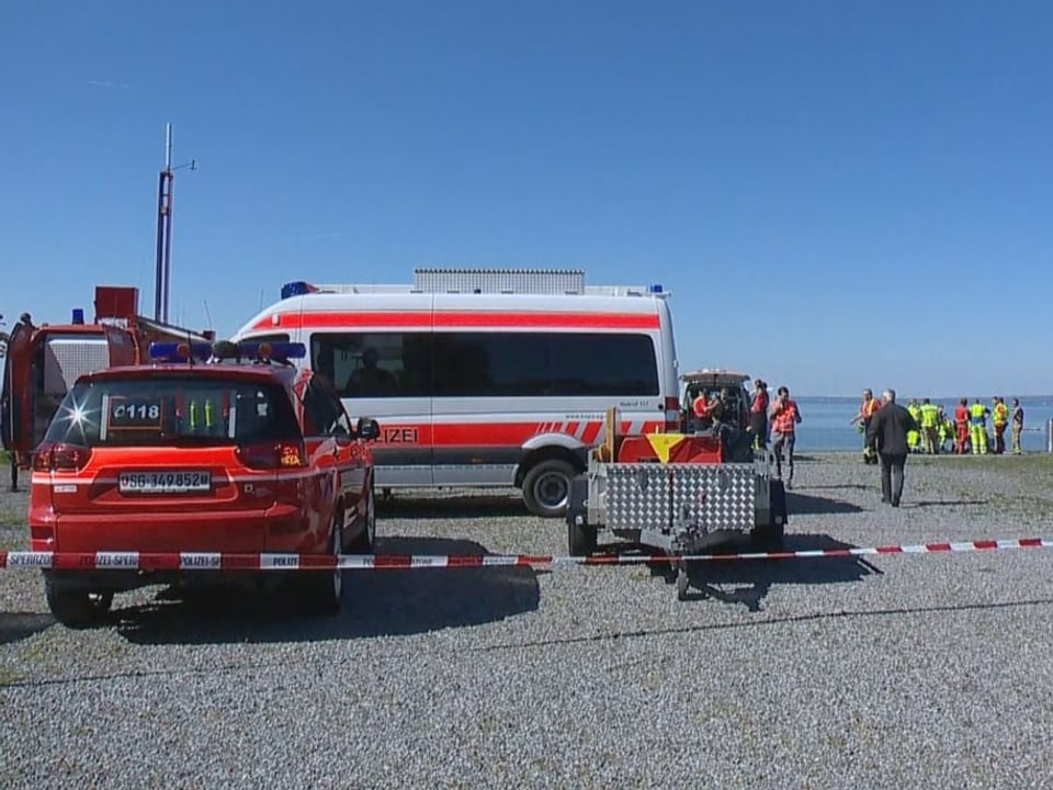 Rettungskräfte und Autos stehen am Ufer vor der Absturzstelle