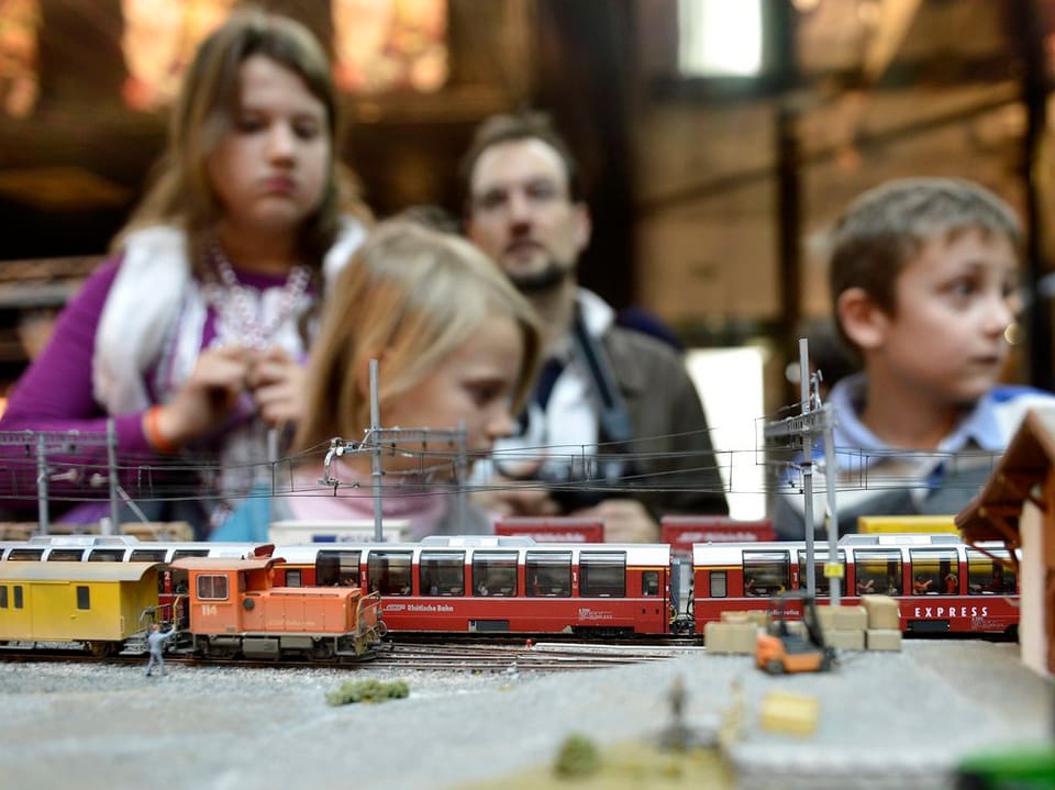 Kinder bestaunen eine Modelleisenbahnanlage, im Vordergrund eine Rangierlokomotive und Panroamawagen eines weiteren Zuges