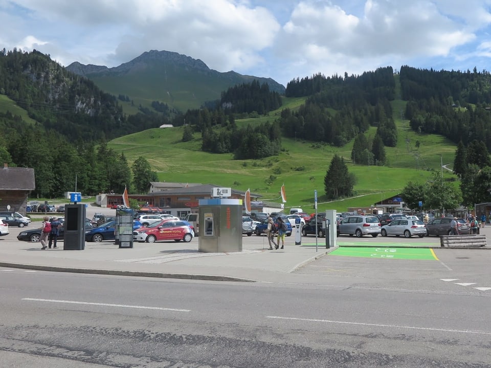 Ein Parkplatz, dahinter grüne Berghänge.