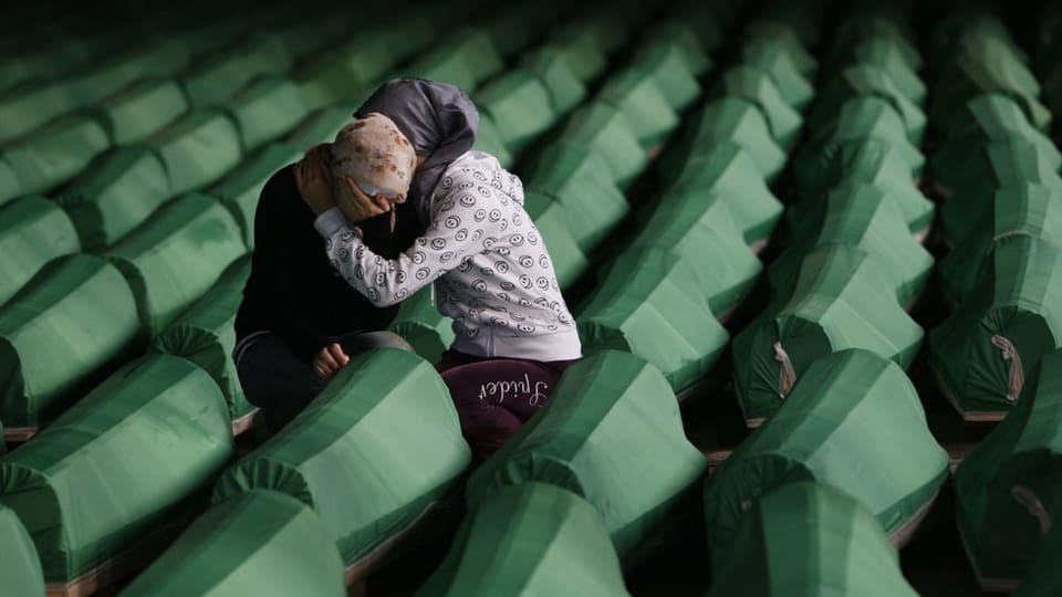 Zwei Frauen trösten sich zwischen Särgen nach dem Völkermord in Srebrenica von 1995.