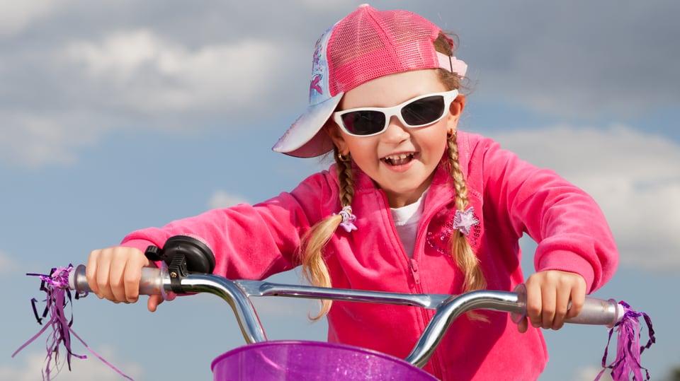 Kleines Mädchen mit Basecap und Sonnenbrille sitzt auf Retro-Fahrrad