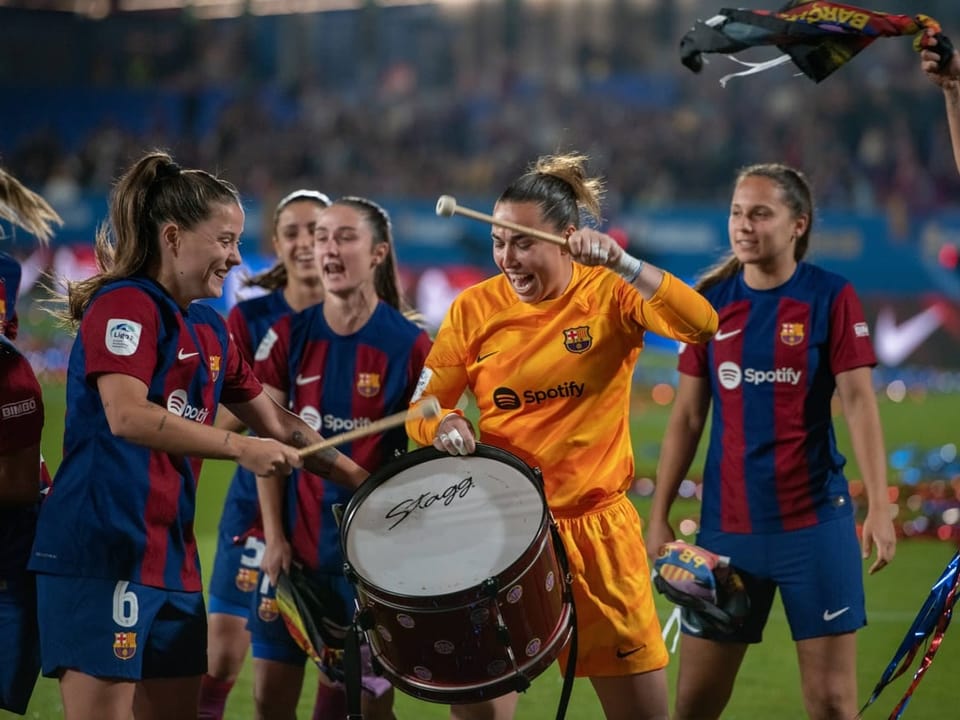 Fussballspielerinnen des FC Barcelona feiern einen Sieg mit einer Trommel auf dem Spielfeld.