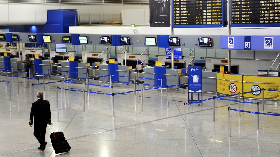 Ein Pilot mit Rollkoffer durchquert die leere Schalterhalle am Athener Flughafen.