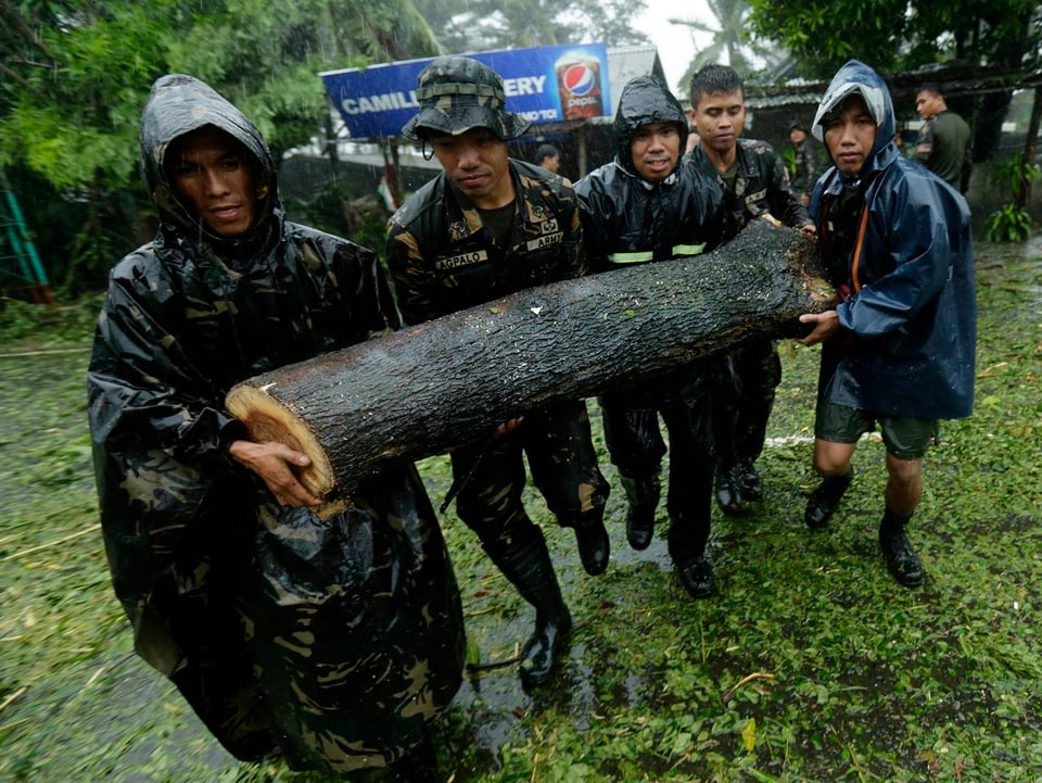 Philippinsche Soldaten tragen einen zersägten Baumstamm von einer mit Ästen und Blättern übersäten Strasse