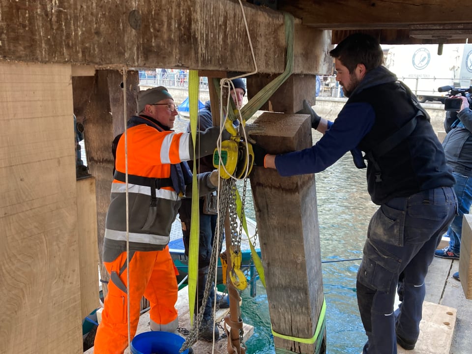 Zwei Arbeiter ziehen den abgesägten Pfosten aus dem Wasser.