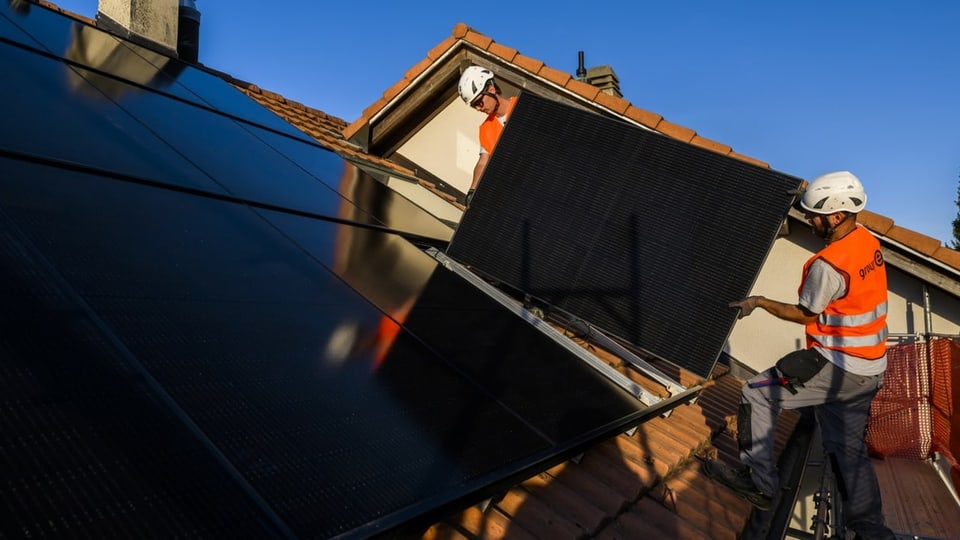 Zwei Fachmänner installieren ein Solarpanel auf einem Hausdach.