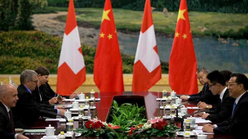Schweizer Vertreter auf der linken Seite eines Tischs, chinesische Verteter auf der rechten Seite, im Hintergrund Schweizer- und Chinafahnen.