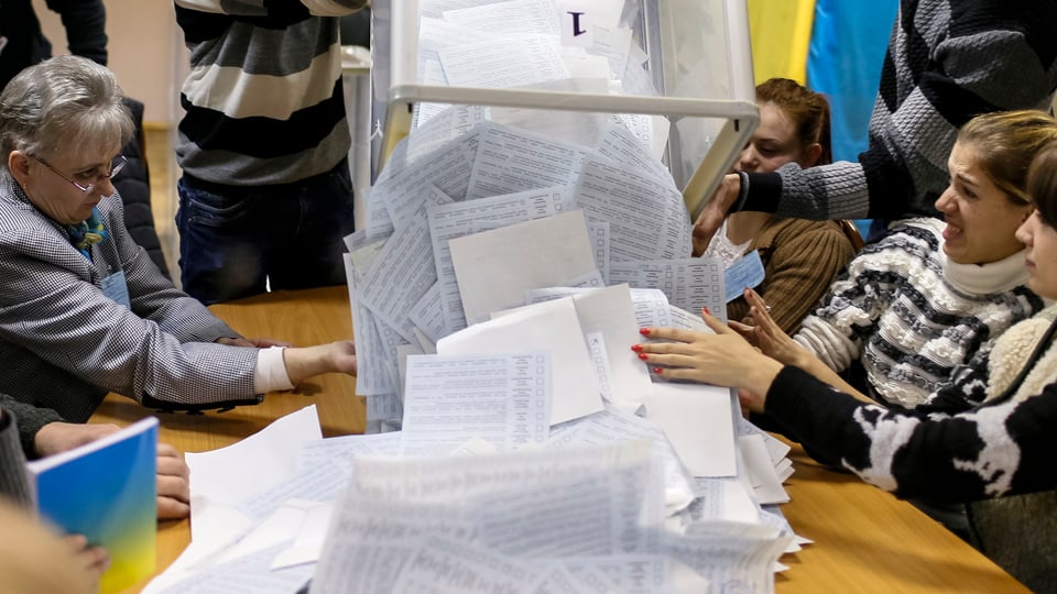 Wahlzettel werden aus einer Urne auf einen Tisch geleert.
