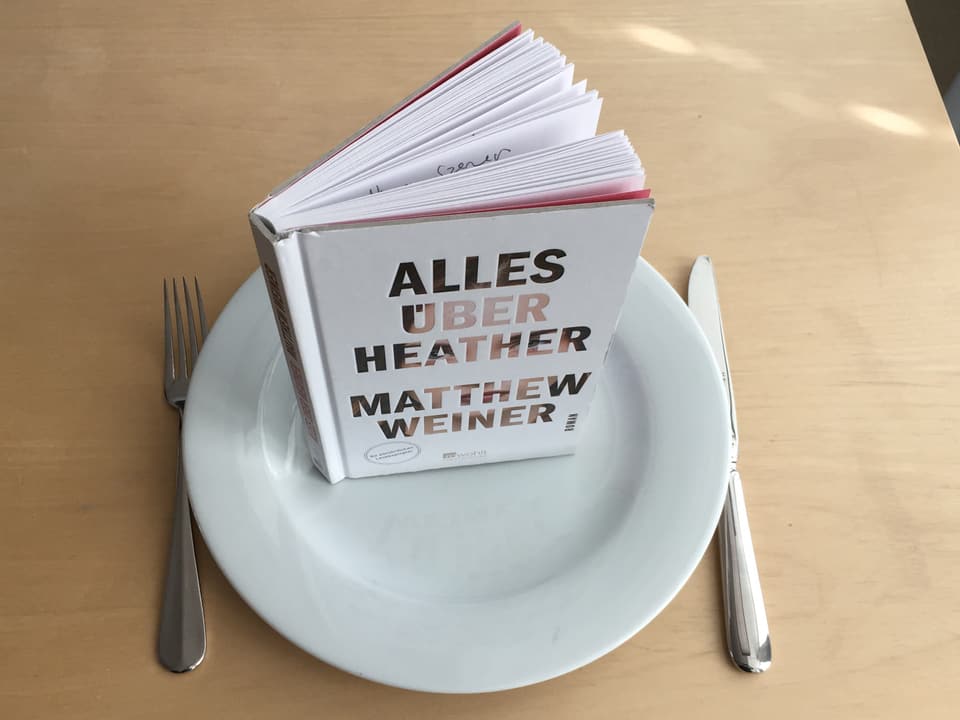 «Alles über Heather» von Matthew Weiner steht auf einem weissen Teller. Meser und Gabel daneben. 