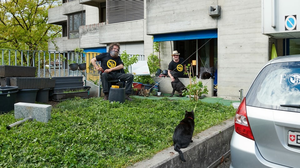Zwei Männer sitzen draussen – mit Katze und Hund.