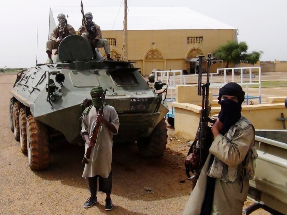 Malische Kämpfer mit Waffen vor einem Schützenpanzer.