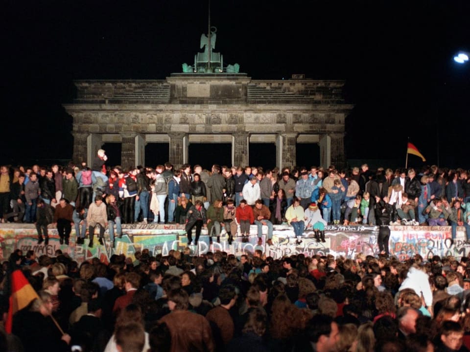 Jubelnde Menschen stehen auf der Berliner Mauer am Brandenburger Tor am. 