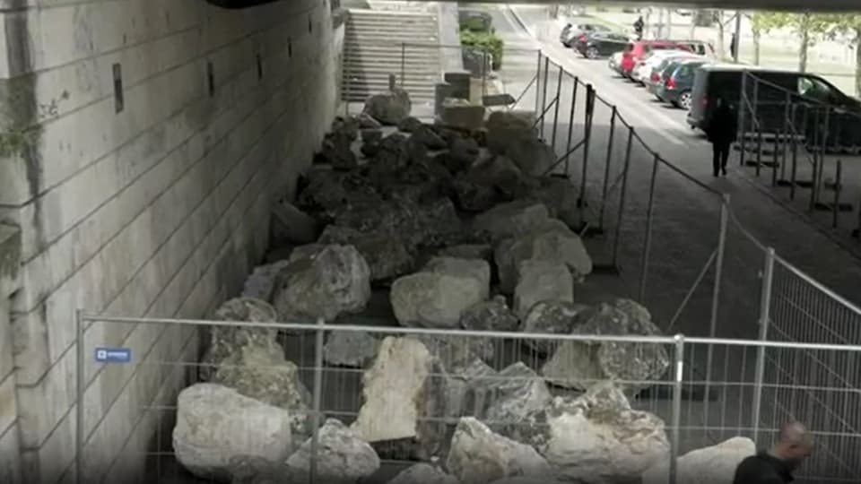 Bauarbeiten im Gange mit einer Absperrung und einem Haufen grosser Steine auf einem städtischen Gehweg.