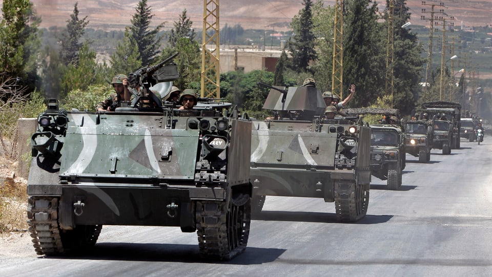 Kolonne aus gepanzerten Armeefahrzeugen mit Soldaten fahren auf einer Strasse.