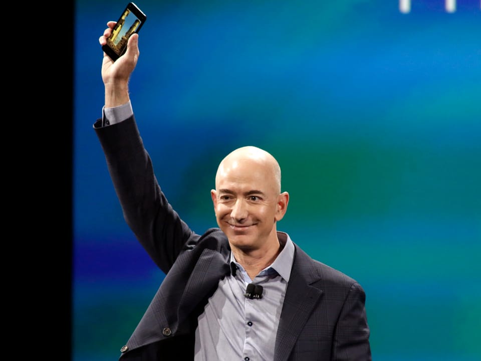 Portrait von Amazon CEO Jeff Bezos, der sein Smartphone zeigt.