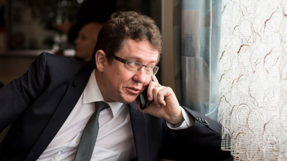 Ein Politiker im Anzug telefoniert am Fenster und blickt nach aussen 