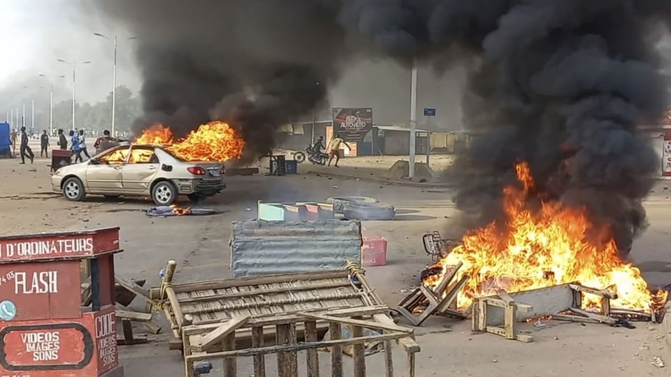 Ein Bild des Chaos – herumlaufende Menschen, brennende Autos mit schwarzem Rauch, Reifen auf der Strasse. 