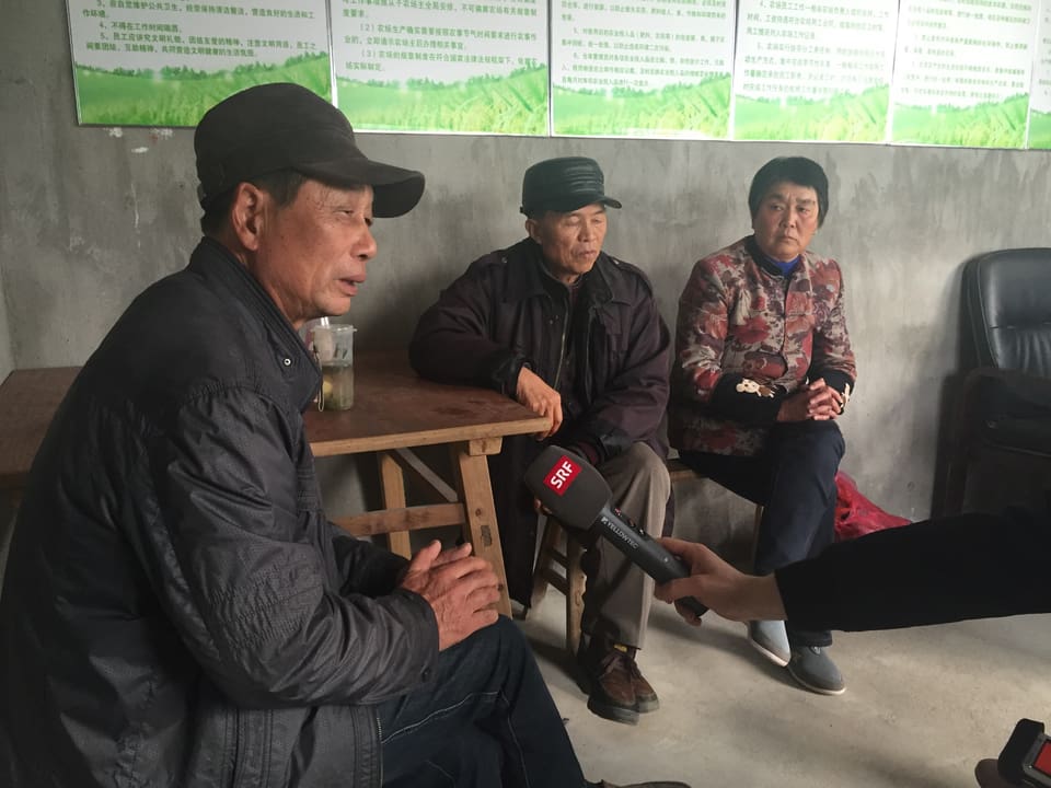 Bauer Gu Meicheng sitzt an einem Tisch. Daneben ein Nachbar und seine Ehefrau.