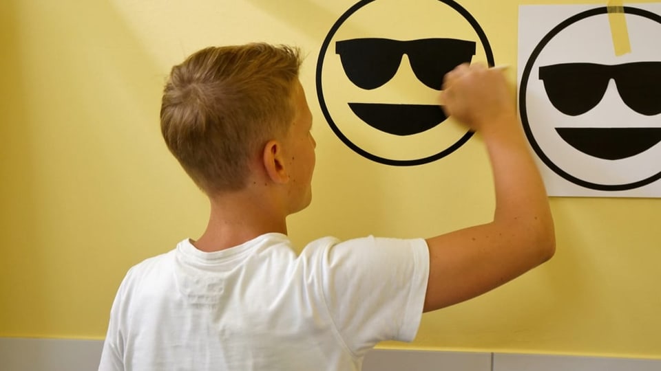 EInjunge malt ein Emoji an eine gelbe Wand