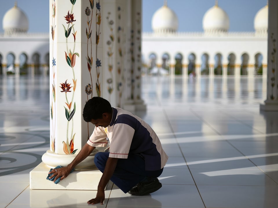 Ein Arbeitsmigrant putzt den Fuss einer Säule im Atrium einer Moschee.