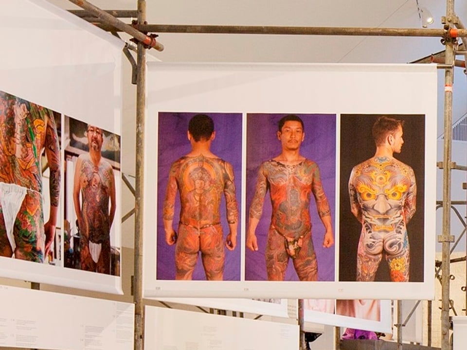 Grossformatige Plakate in der Ausstellung zeigen tätowierten Mann von allen Seiten. 