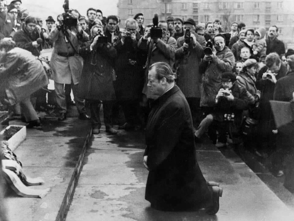 Willy Brandt kniet auf einer Treppe, neben ihm viele Presseleute